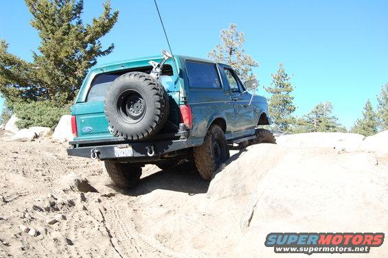 Green Ford Bronco climbing over rocks on a dirt trail. Spare tire mounted on rear