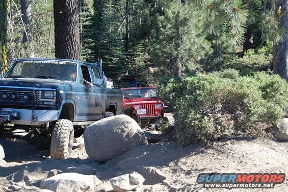 Red Jeep Wrangler on a dirt trail with a blue pickup truck