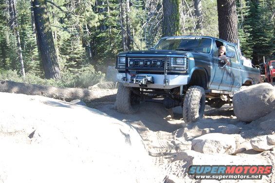 Blue pickup truck with aftermarket bumper and winch navigating rocks