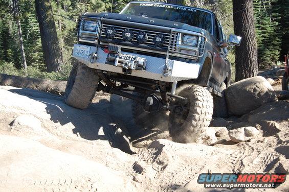 Front view of a dark off-road truck with a winch and auxiliary lights navigating rocks
