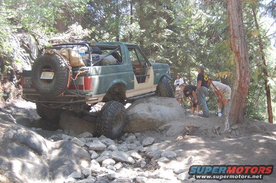Green and tan 1993 Ford Bronco off-roading on rocks, rear spare tire visible