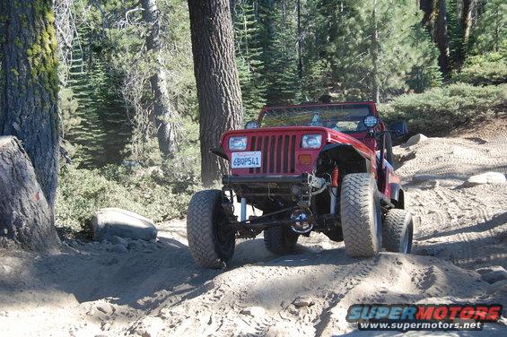 Red Jeep Wrangler on a dirt trail, front view, lifted suspension, large tires, California license plate
