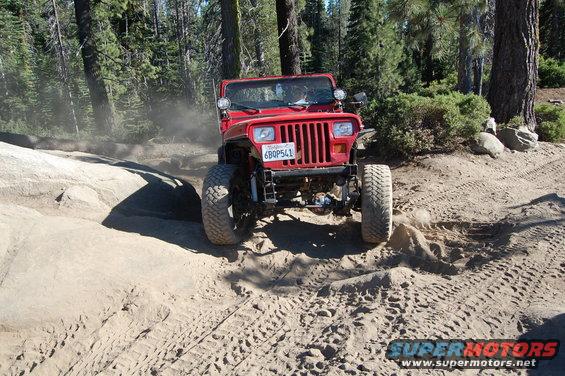 Red 1993 Jeep Wrangler driving on a dirt trail with trees and rocks