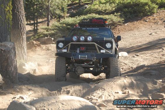 Modified off-road truck with winch and roof rack driving on a dirt trail