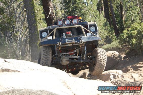 Modified off-road vehicle with large tires and a brush guard navigating a rocky trail