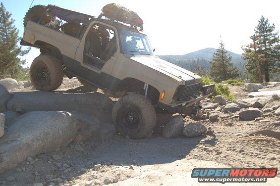 Tan SUV with large tires climbing over rocks on a dirt trail