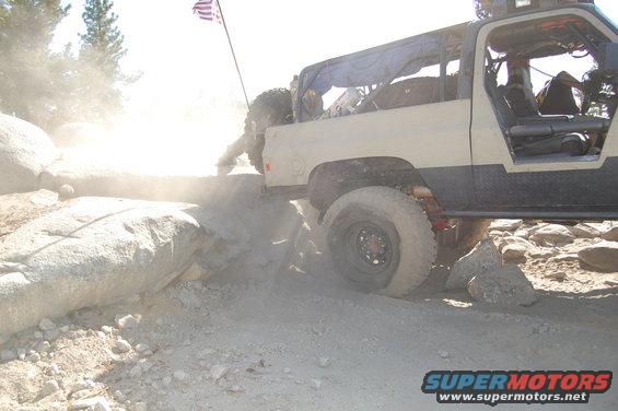 Off-road truck with an American flag on a pole is going over rocks, kicking up dust