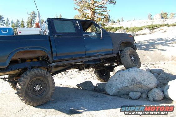 Dark blue pickup truck with large tires on rocks, front right tire elevated