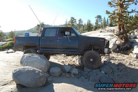Dark blue crew cab pickup truck with large tires navigating rocky terrain