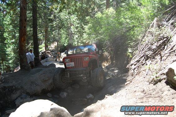 Red 1993 Jeep Wrangler navigating a rocky, wooded trail