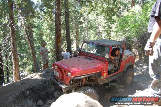 Red 1993 Jeep Wrangler navigating a rocky, wooded trail