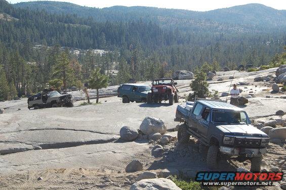 Several off-road vehicles navigate a rocky, mountainous landscape under a clear sky