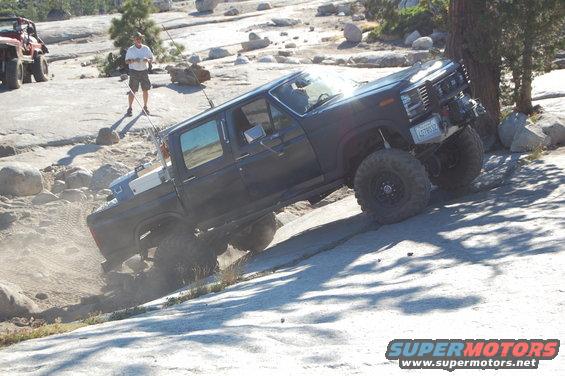 Dark blue lifted pickup truck off-roading on rocks, license plate visible