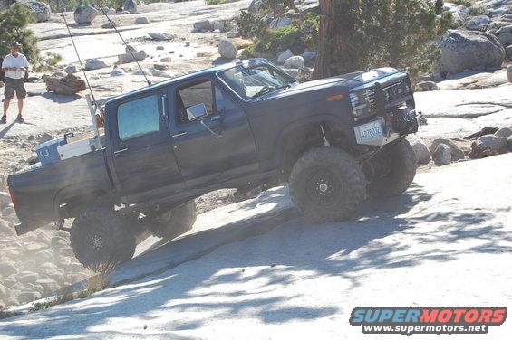 Dark blue crew cab pickup truck with large tires climbing a rocky incline. License plate reads LDT8032