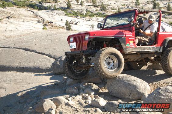 Red 1993 Jeep Wrangler off-roading over rocks, front passenger side tire elevated