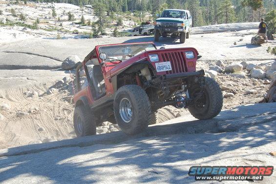 Red Jeep Wrangler climbing over rocks on a trail, with a green Ford Bronco and another vehicle behind it