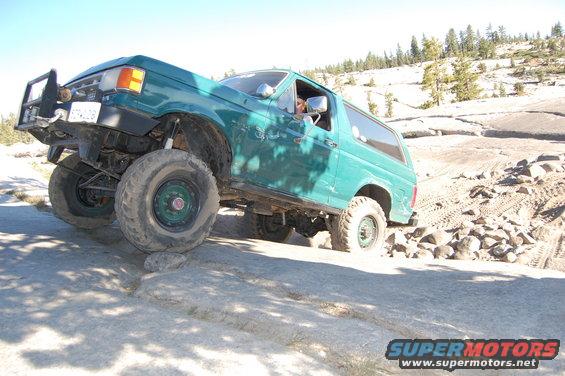 Green Ford Bronco with aftermarket bumper and large tires navigating a rocky trail