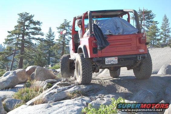 Red Jeep Wrangler driving over rocks on a trail. License plate reads 6BQP541