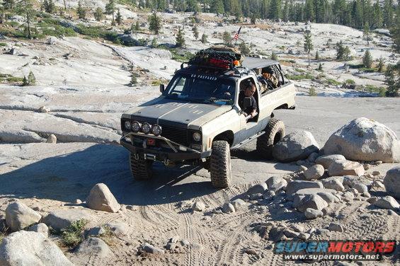 Modified pickup truck with roof rack and off-road tires navigating rocky terrain