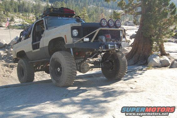 Modified Chevrolet K5 Blazer with large tires and off-road lights, parked on rocky terrain