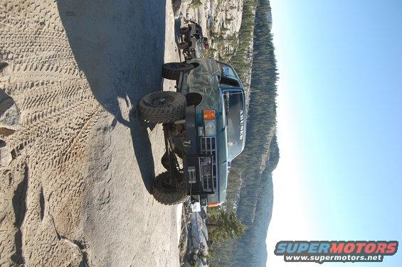 Green off-road SUV with large tires on a rocky mountain trail. Text on windshield reads 'AHUNED'