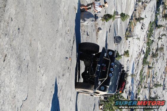 Jeep Wrangler parked on a steep, rocky incline with a person sitting nearby