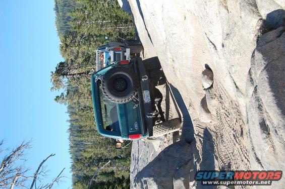 Green Ford Bronco climbing a steep rock face with another vehicle behind it
