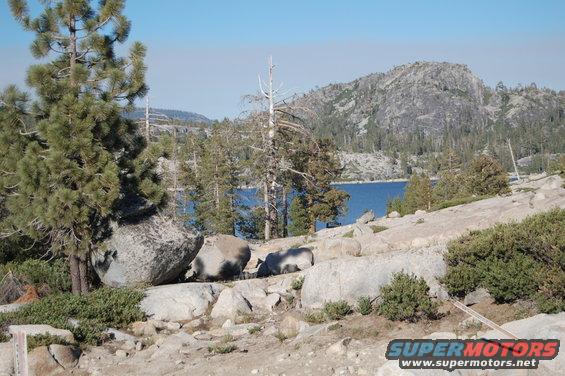 Rocky terrain with pine trees and a blue lake in the background
