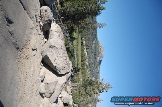 Tire tracks on rocky terrain with trees and mountains in background