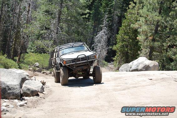 White off-road vehicle with roll cage and large tires on a dirt path