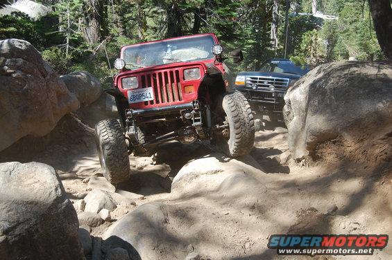Red 1993 Jeep Wrangler navigating a rocky trail with a black SUV behind it