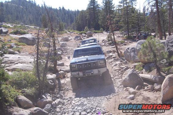 Several off-road vehicles driving on a rocky trail through a forest