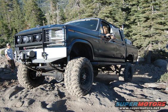 Black lifted pickup truck with custom bumper and winch, driving on a rocky trail