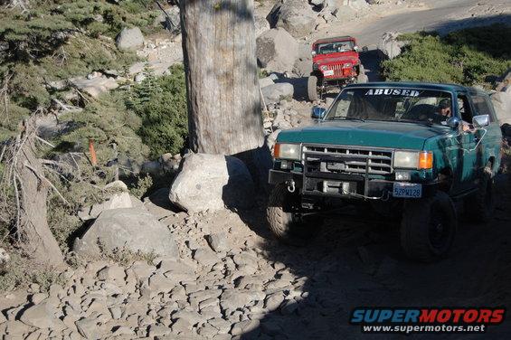 Green SUV with "ABUSED" sticker on windshield driving on a rocky trail