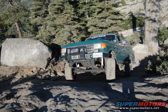 Green Ford F-150 off-roading on a rocky trail, front bumper modified with a winch. License plate reads 52PW128