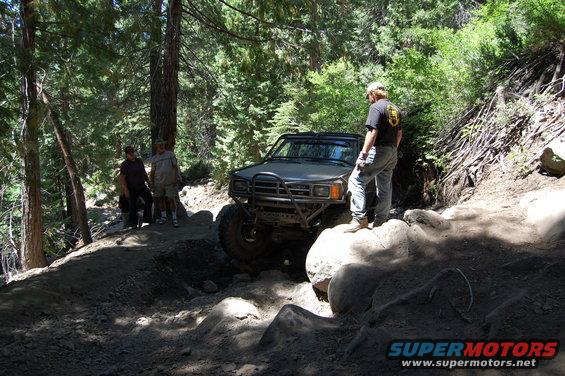 Gray off-road SUV navigating a rocky trail with people watching