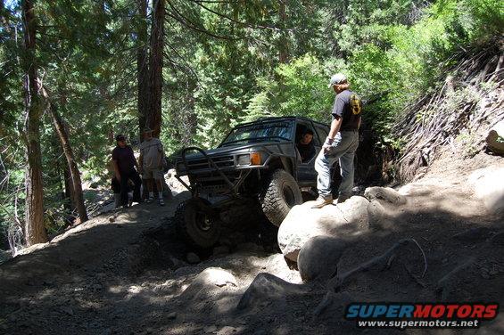 off-road vehicle climbing over rocks on a dirt trail with trees around