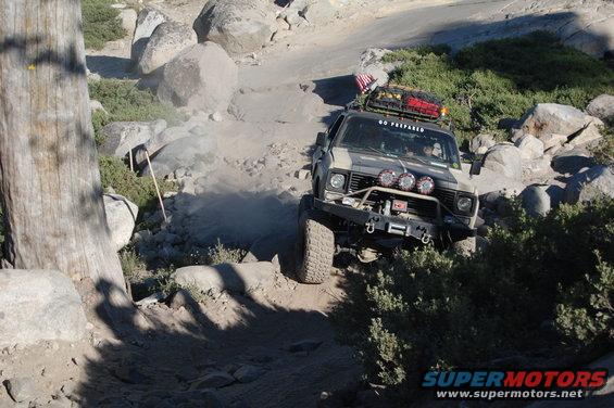 Gray Jeep CJ-7 off-roading on a rocky trail, with a winch and extra lights