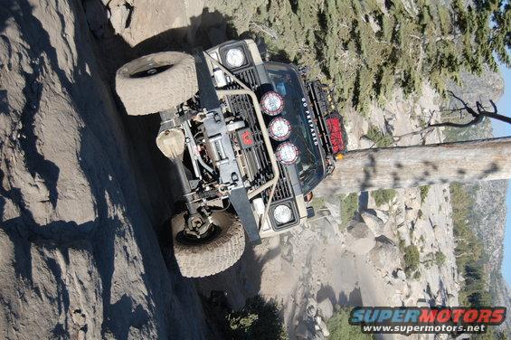 Tan off-road vehicle with winch and lights climbing a steep, rocky trail