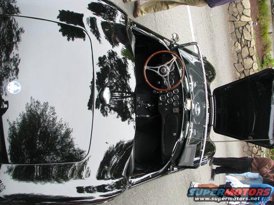 Black classic convertible interior with wood steering wheel and multiple gauges. Hood is open