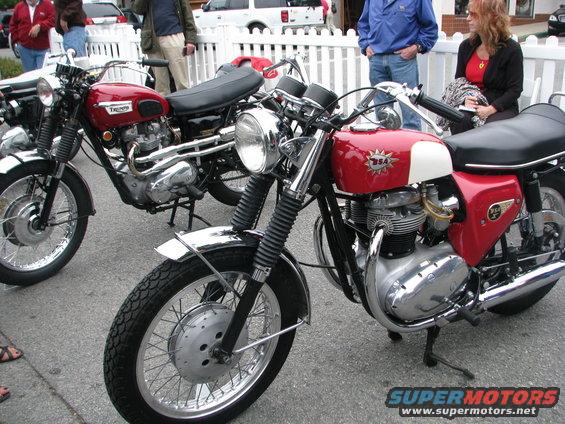 Two vintage motorcycles parked on pavement, one red and white BSA, another red Triumph