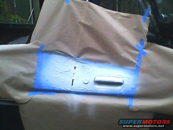 Car door panel covered in masking paper and blue tape, ready for paint
