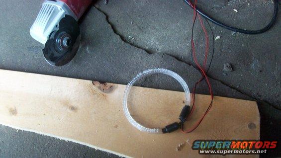Angle grinder and a clear LED ring light with black connectors and red wires on a wooden plank