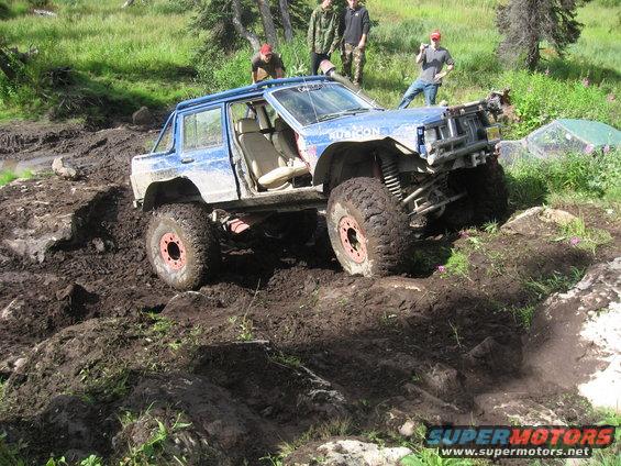 Blue off-road jeep with large tires navigating a muddy trail
