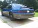 1989 Ford Mustang - A blue coupe car is parked on a driveway, showing its rear and side profile with a spoiler and grey lower body.
