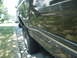 1988 Ford Bronco - A dark green Ford Bronco is parked on the side of a residential street, showing its side profile and tire.