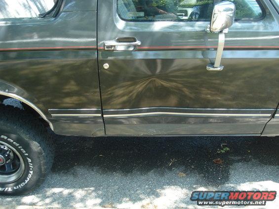 Dark gray SUV side door with a dent and chrome trim. A red stripe runs above the trim