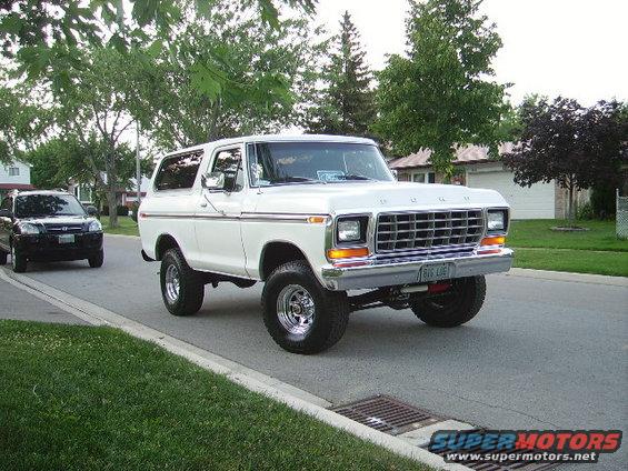 White 1978 Ford Bronco with chrome wheels and a chrome grille, seen from a 3/4 front angle on a residential street