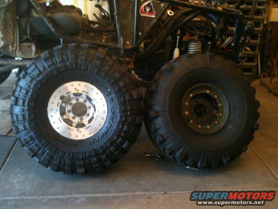 Two large off-road tires, one with a silver rim, next to a vehicle chassis