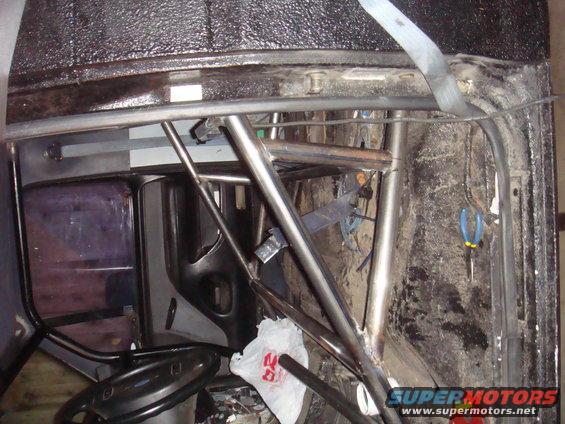Interior of a vehicle with a metal roll cage, steering wheel, and dark tinted window